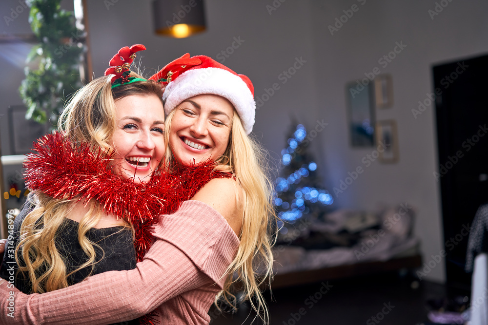 Two hugging women with tinsel during celebration of Christmas in apartment. Two hugging women with tinsel during celebration of Christmas in apartment.