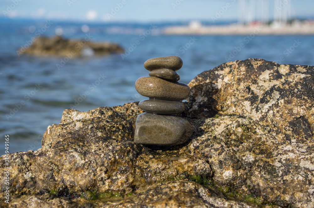 Five stones cairn tower, rock zen sculpture, brown beige pebbles on the rock and sea light blue background