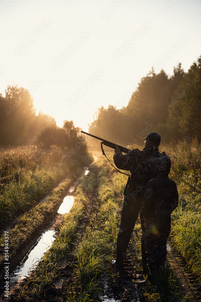 Hunters with hunting equipment going away through rural field towards forest at sunset during hunting season in countryside. Hunters with hunting equipment going away through rural field towards forest at sunset during hunting season in countryside.