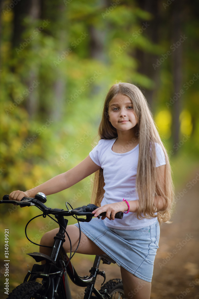 Cute little teenager girl riding bicycle in a sunny park