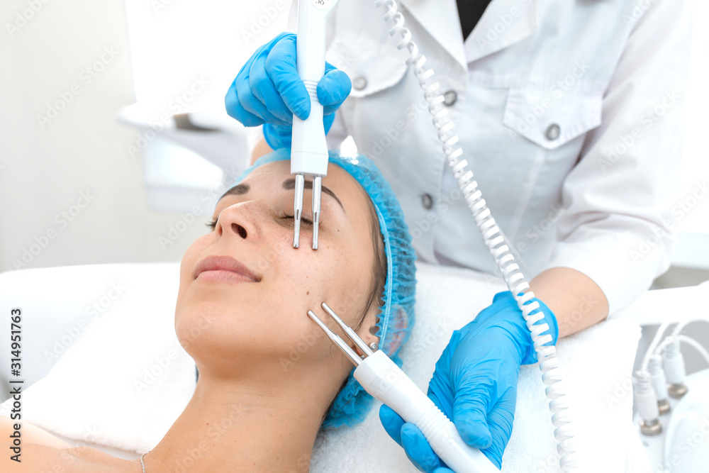 Portrait of a young beautiful girl face microcurrent therapy procedure. Facial care and rejuvenation. Increase epidermal tone Portrait of a young beautiful girl face microcurrent therapy procedure. Facial care and rejuvenation. Increase epidermal tone