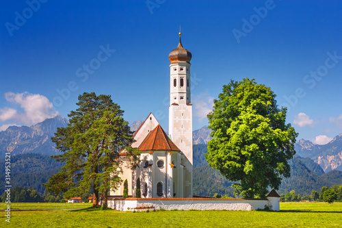 Bavarian landscape - view of the church of St. Coloman on the background of the Alpine mountains in summer day, Germany photo