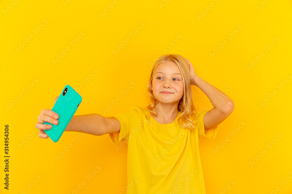 Smiling little girl kid showing blue screen of new popular mobile phone on light yellow background Smiling little girl kid showing blue screen of new popular mobile phone on light yellow background
