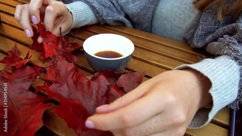 Close-up of a girl's hand playing leaves near to a cup of coffee on a table