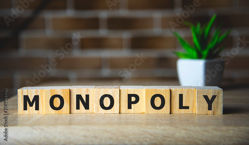 Monopoly written on a wooden cube on brick background.