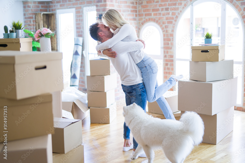 Fototapeta premium Young beautiful couple with dog hugging at new home around cardboard boxes