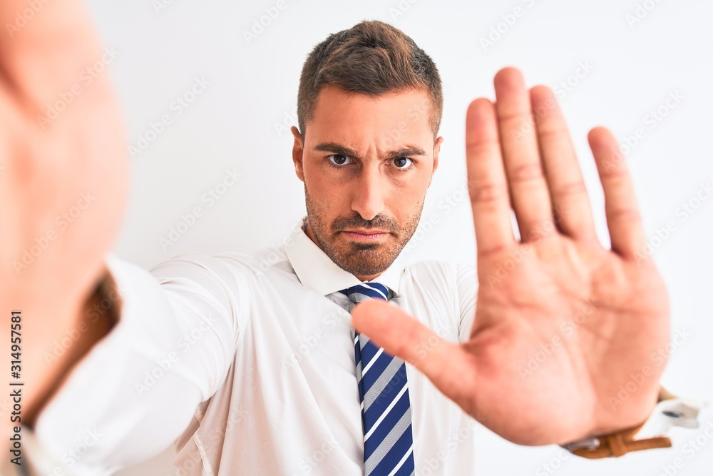 Young handsome business man taking selfie using smartphone over isolated background with open hand doing stop sign with serious and confident expression, defense gesture Young handsome business man taking selfie using smartphone over isolated background with open hand doing stop sign with serious and confident expression, defense gesture