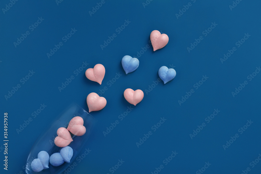 pink and one blue meringue hearts in transparent glass goblet and scattered on classic blue background diagonally, copy space pink and one blue meringue hearts in transparent glass goblet and scattered on classic blue background diagonally, copy space
