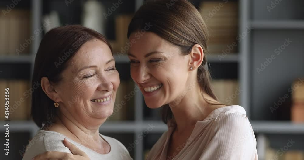 Affectionate 60s mum and 30s daughter looking at camera hugging Affectionate 60s mum and 30s daughter looking at camera hugging