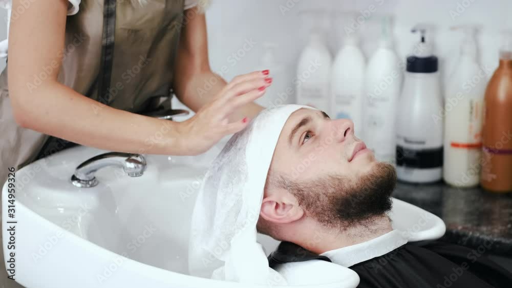 A towel is white. A client has a beard. A hairdresser is washing client's head. A towel is white. A client has a beard. A hairdresser is washing client's head.