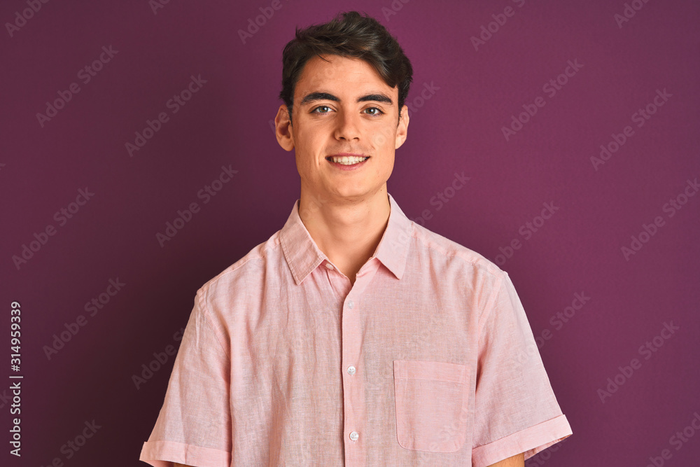 Fototapeta premium Teenager boy wearing pink shirt standing over purple isolated background looking away to side with smile on face, natural expression. Laughing confident.