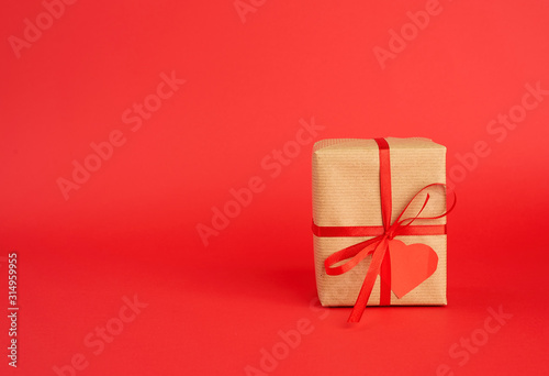 wrapped square box with a gift in brown craft paper and tied with a thin silk red ribbon