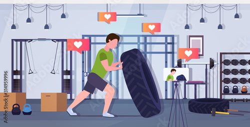 fitness blogger flipping a tire trainer streaming live recording video with smartphone camera on tripod sport activity workout blogging healthy lifestyle concept gym interior horizontal full length