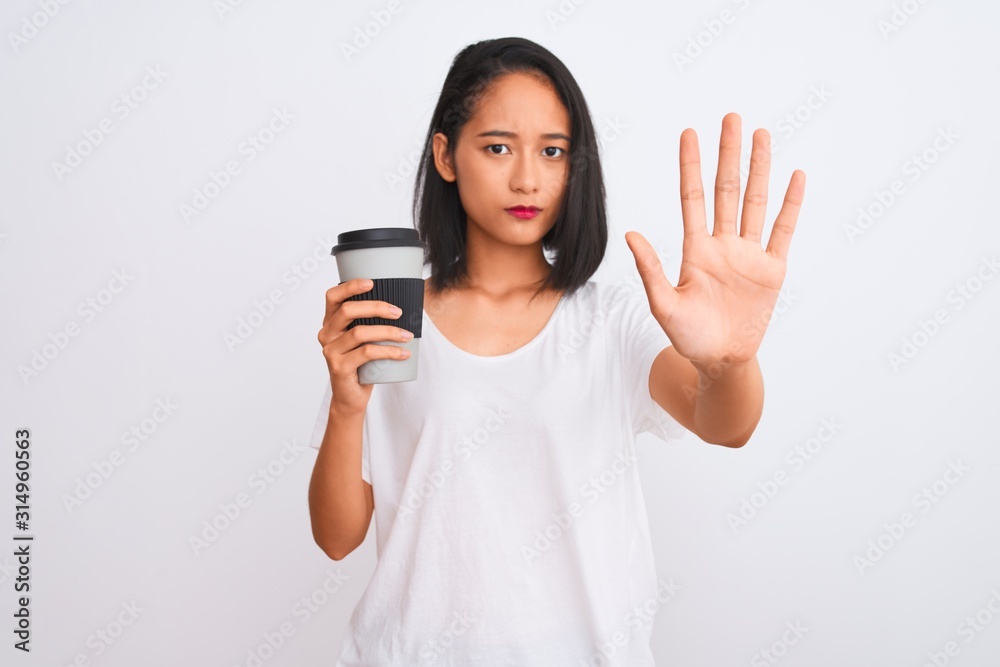 Young chinese woman drinking take away glass of coffee over isolated white background with open hand doing stop sign with serious and confident expression, defense gesture Young chinese woman drinking take away glass of coffee over isolated white background with open hand doing stop sign with serious and confident expression, defense gesture