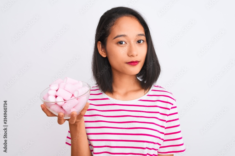 Beautiful chinese woman holding bowl with marshmallows over isolated white background with a confident expression on smart face thinking serious Beautiful chinese woman holding bowl with marshmallows over isolated white background with a confident expression on smart face thinking serious