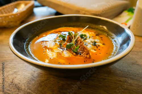orange thick pumpkin soup in a brown clay plate on a dark wooden table, the dish is decorated with croutons and fresh herbs, a delicious background for the menu 