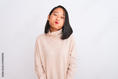 Young chinese woman wearing turtleneck sweater standing over isolated white background puffing cheeks with funny face. Mouth inflated with air, crazy expression.