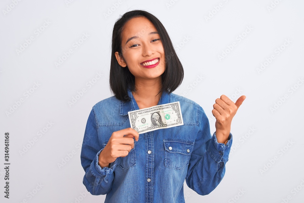 Young beautiful chinese woman holding one dollar standing over isolated white background happy with big smile doing ok sign, thumb up with fingers, excellent sign Young beautiful chinese woman holding one dollar standing over isolated white background happy with big smile doing ok sign, thumb up with fingers, excellent sign