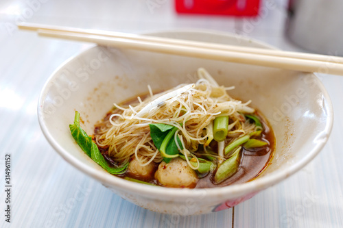 Close up view of Spicy Thai Boat rice Noodle Soup,  Kuai Tiao Ruea, serve on ceramic bowl on white wooden table.  photo