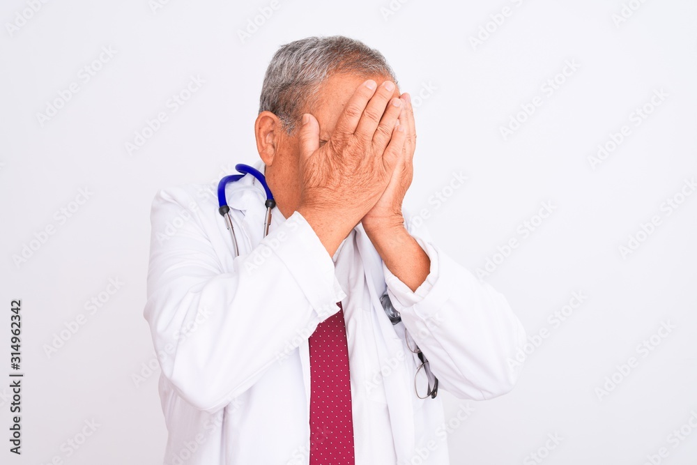 Senior grey-haired doctor man wearing stethoscope standing over isolated white background with sad expression covering face with hands while crying. Depression concept. Senior grey-haired doctor man wearing stethoscope standing over isolated white background with sad expression covering face with hands while crying. Depression concept.
