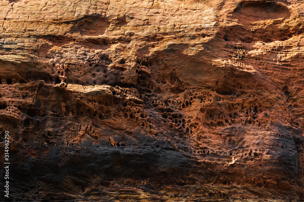 Rocks from black and orange sandstone with traces of destruction, erosion. Abstract stone texture