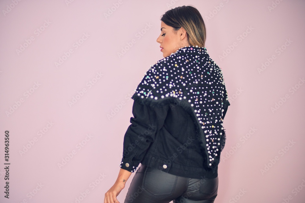 Young beautiful woman wearing fashionable clothes standing backwards over isolated pink background Young beautiful woman wearing fashionable clothes standing backwards over isolated pink background
