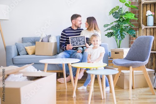 Beautiful famiily with kid sitting on the sofa holding blackboard at new home around cardboard boxes