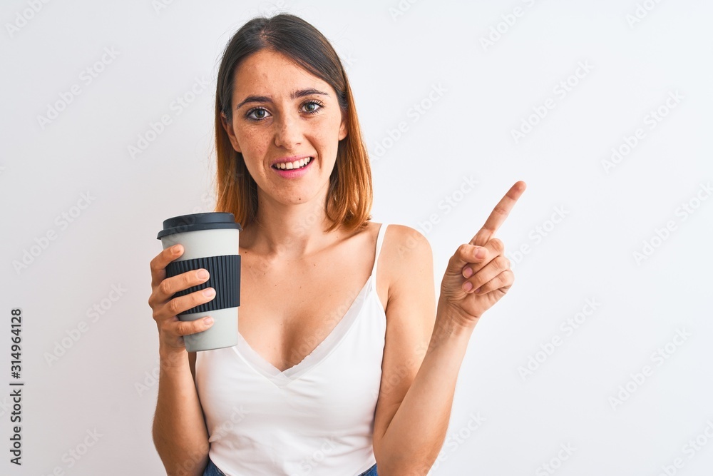 Beautiful redhead woman drinking take away coffee over isolated background very happy pointing with hand and finger to the side Beautiful redhead woman drinking take away coffee over isolated background very happy pointing with hand and finger to the side