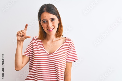 Beautiful redhead woman wearing casual striped red t-shirt over isolated background smiling and confident gesturing with hand doing small size sign with fingers looking and the camera. Measure