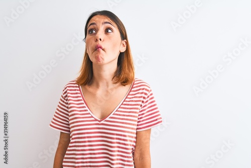 Beautiful redhead woman wearing casual striped red t-shirt over isolated background making fish face with lips, crazy and comical gesture. Funny expression.