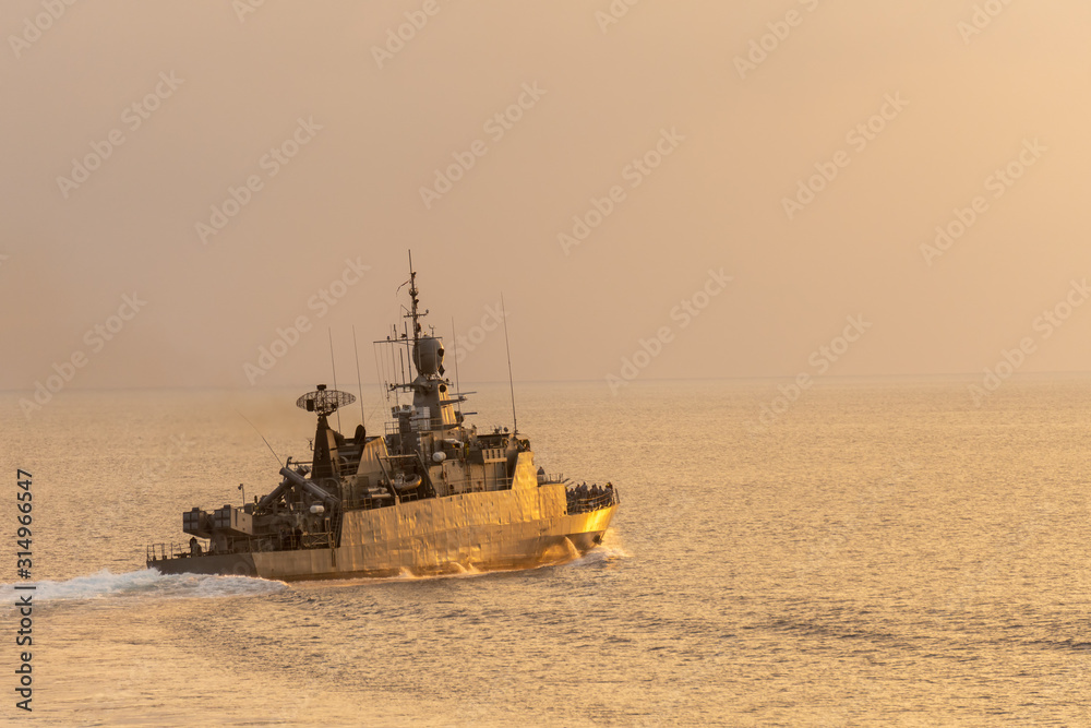 Silhouette of Navy corvette sails in the sea with golden light brace upon the sea surface.