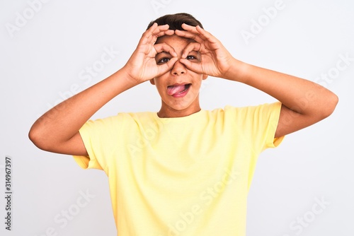 Handsome teenager boy standing over white isolated background doing ok gesture like binoculars sticking tongue out, eyes looking through fingers. Crazy expression.