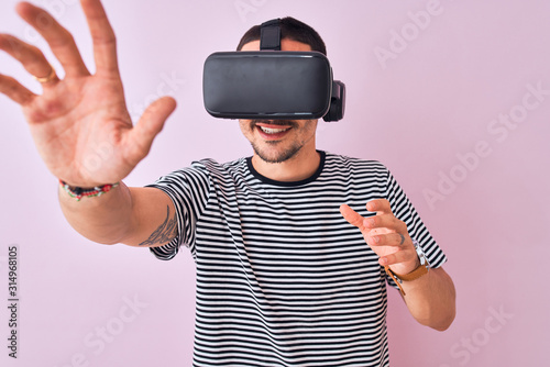 Young man playing video game wearing virtual reality glasses  looking at virtual simulation amazed and smiling happy