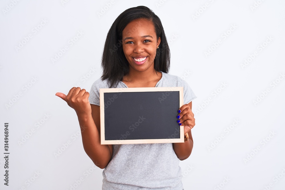 Young african american woman holding blank school blackboard over isolated background pointing and showing with thumb up to the side with happy face smiling Young african american woman holding blank school blackboard over isolated background pointing and showing with thumb up to the side with happy face smiling