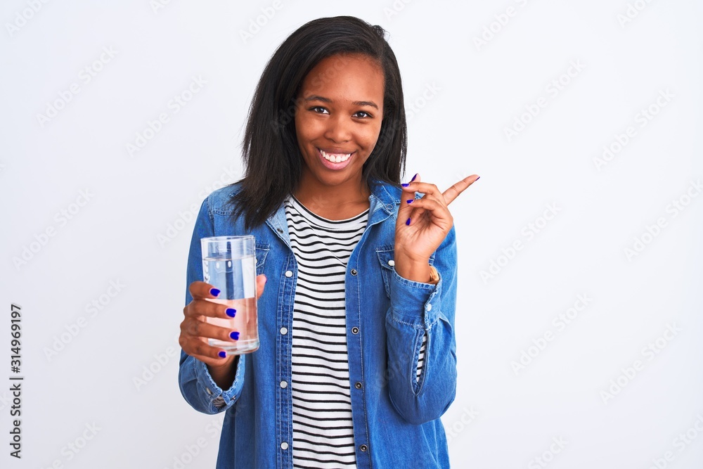 Young african american woman drinking a glass of fresh water over isolated background very happy pointing with hand and finger to the side Young african american woman drinking a glass of fresh water over isolated background very happy pointing with hand and finger to the side