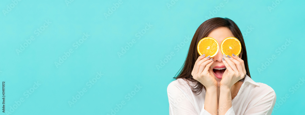 Woman with sliced oranges at the eyes on light blue banner background