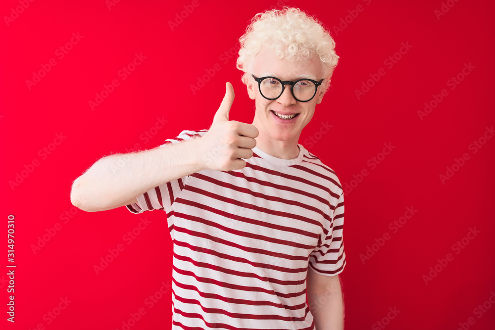 Φωτογραφία Young albino blond man wearing striped t-shirt and glasses over isolated red background doing happy thumbs up gesture with hand