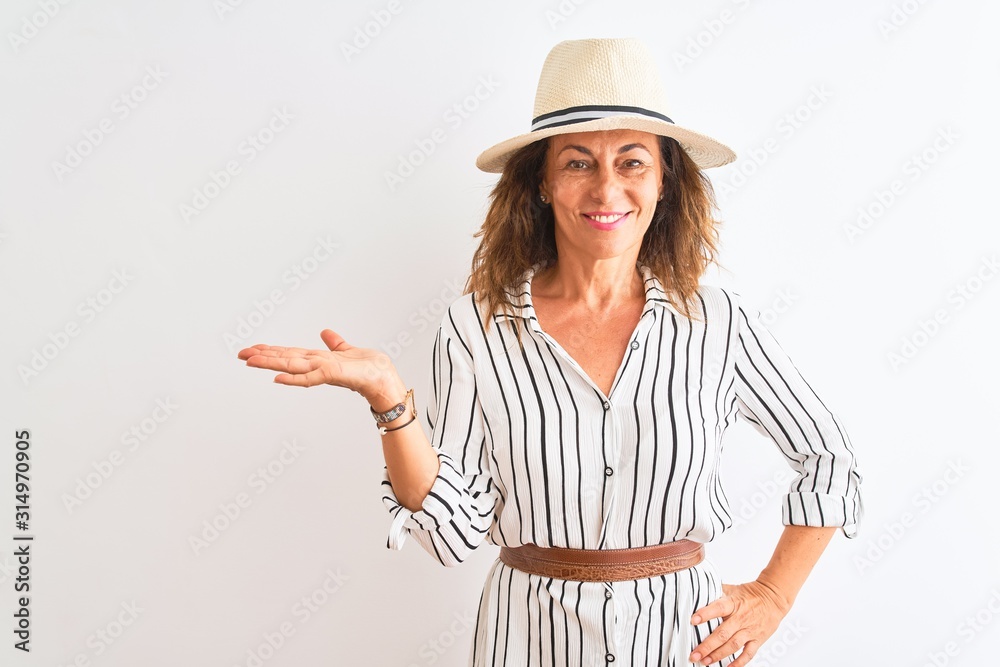 Middle age businesswoman wearing striped dress and hat over isolated white background smiling cheerful presenting and pointing with palm of hand looking at the camera. Middle age businesswoman wearing striped dress and hat over isolated white background smiling cheerful presenting and pointing with palm of hand looking at the camera.