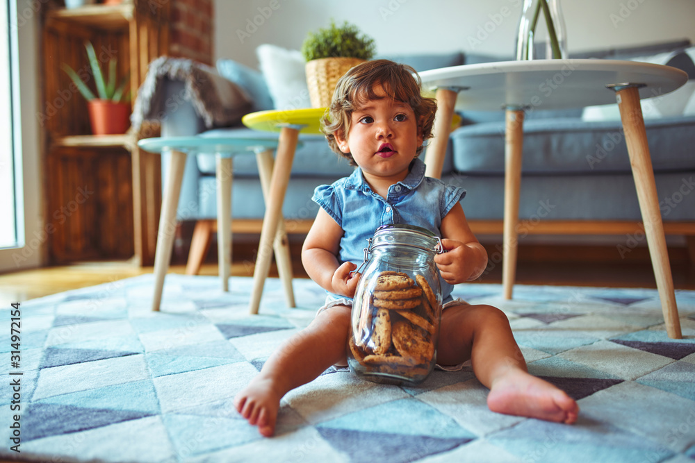 Beautiful toddler child girl holding jar of cookies sitting on the floor - obrazy, fototapety, plakaty 