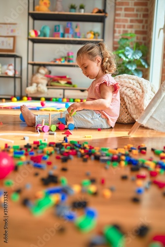 Beautiful blond toddler girl playing with train at kindergarten