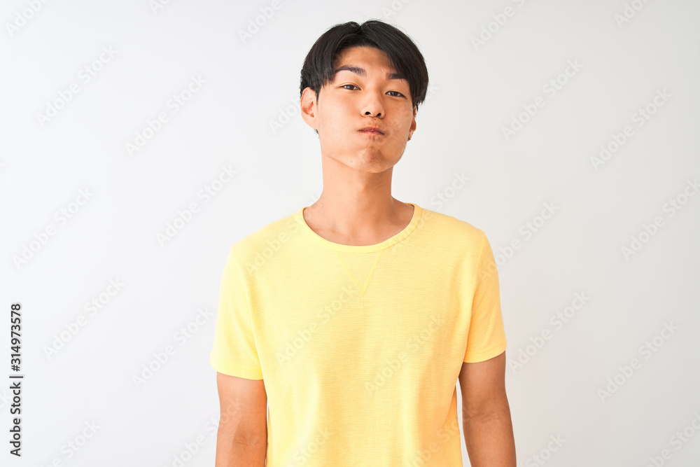 Chinese man wearing yellow casual t-shirt standing over isolated white background puffing cheeks with funny face. Mouth inflated with air, crazy expression. Chinese man wearing yellow casual t-shirt standing over isolated white background puffing cheeks with funny face. Mouth inflated with air, crazy expression.