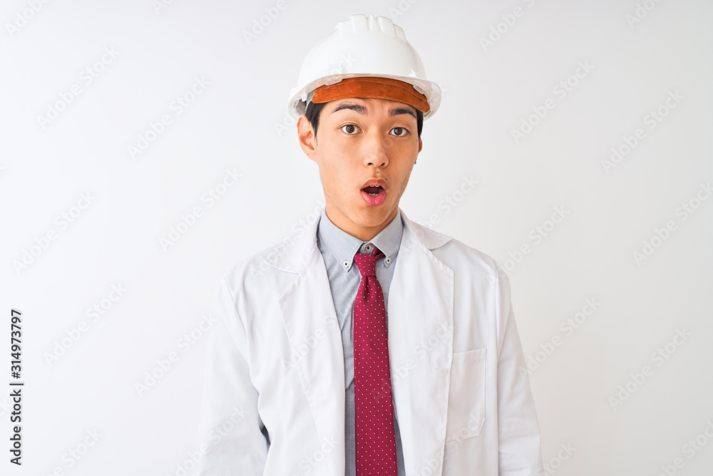 Chinese architect man wearing coat and helmet standing over isolated white background afraid and shocked with surprise expression, fear and excited face. Chinese architect man wearing coat and helmet standing over isolated white background afraid and shocked with surprise expression, fear and excited face.