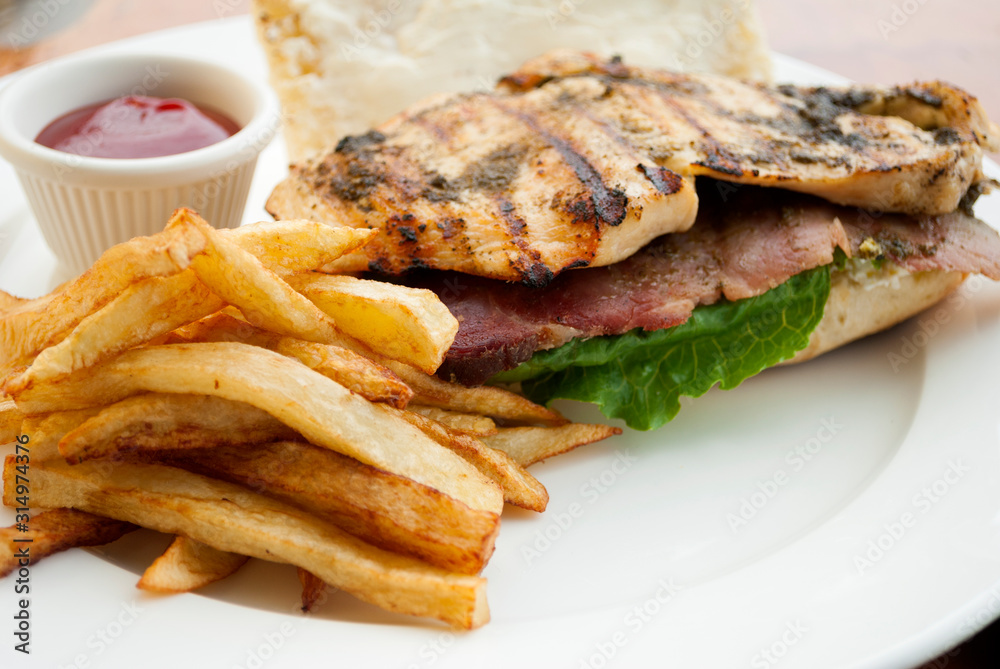 Sandwich prepared with grilled chicken with roast beef, french fries and tomato sauce, served outdoors on wooden table in Guatemala. Sandwich prepared with grilled chicken with roast beef, french fries and tomato sauce, served outdoors on wooden table in Guatemala.