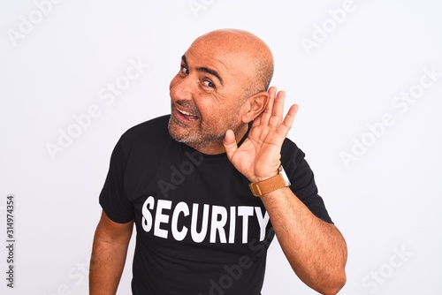 Middle age safeguard man wearing security uniform standing over isolated white background smiling with hand over ear listening an hearing to rumor or gossip. Deafness concept.