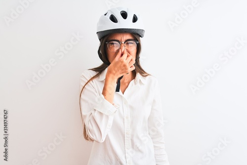 Beautiful businesswoman wearing glasses and bike helmet over isolated white background smelling something stinky and disgusting, intolerable smell, holding breath with fingers on nose. Bad smells  © Krakenimages.com