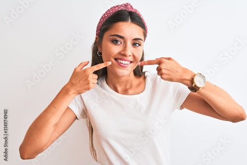 Young beautiful woman wearing casual t-shirt and diadem over isolated white background smiling cheerful showing and pointing with fingers teeth and mouth. Dental health concept. © Krakenimages.com