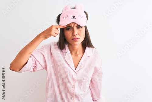 Young beautiful woman wearing sleep mask and pajama over isolated white background pointing unhappy to pimple on forehead, ugly infection of blackhead. Acne and skin problem © Krakenimages.com