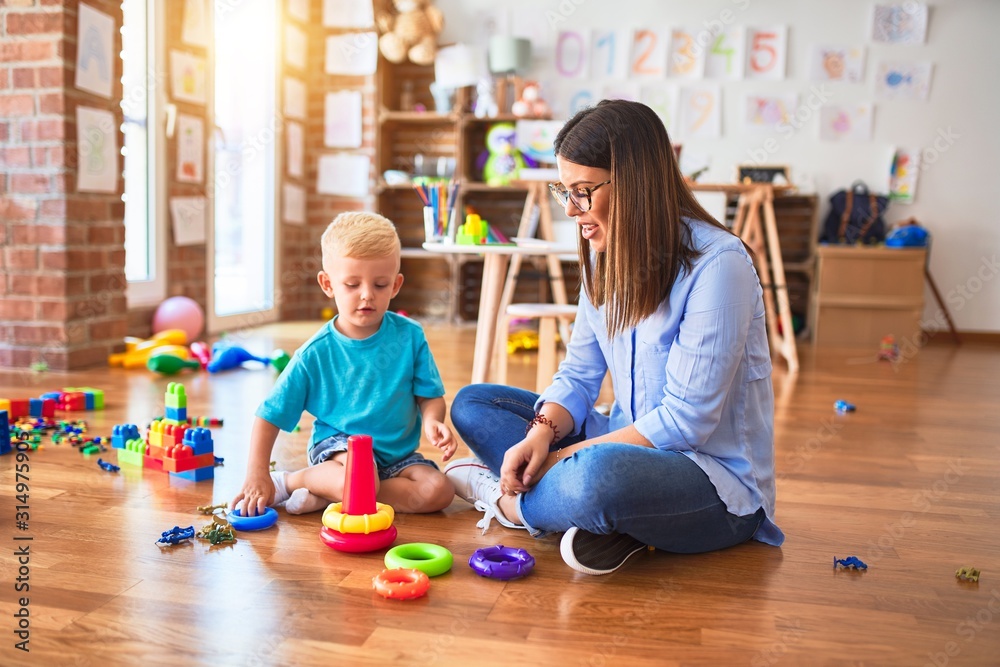 Fototapeta premium Young caucasian child playing at playschool with teacher. Mother and son at playroom with intelligence toy
