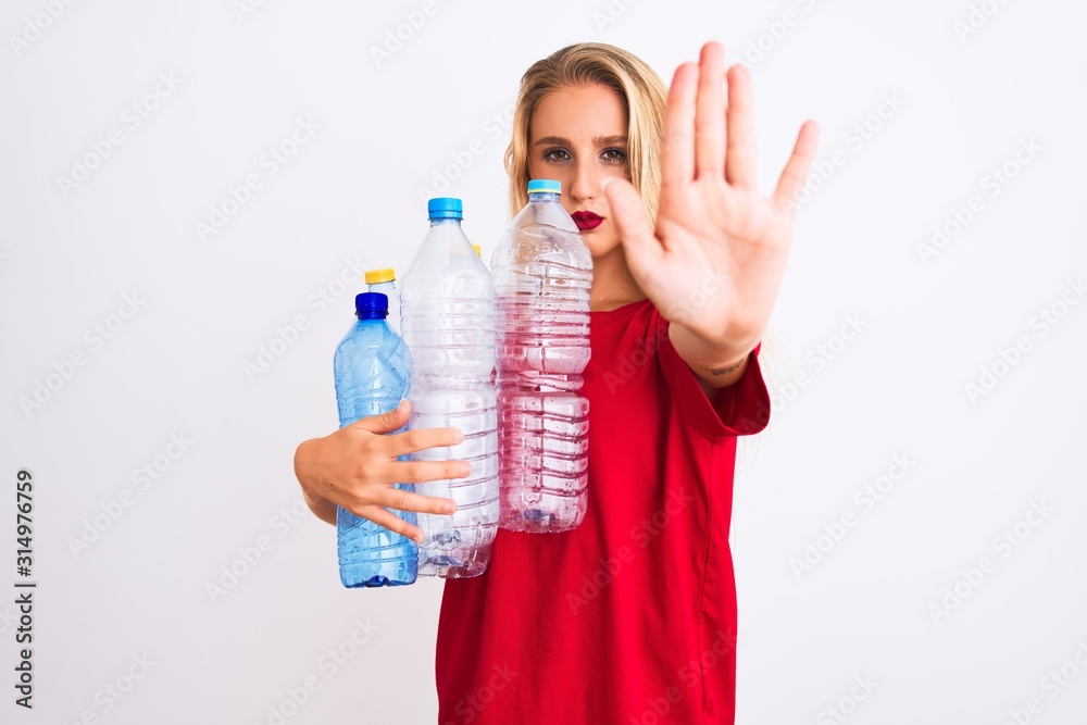 Young beautiful woman recycling plastic bottles standing over isolated white background with open hand doing stop sign with serious and confident expression, defense gesture Young beautiful woman recycling plastic bottles standing over isolated white background with open hand doing stop sign with serious and confident expression, defense gesture
