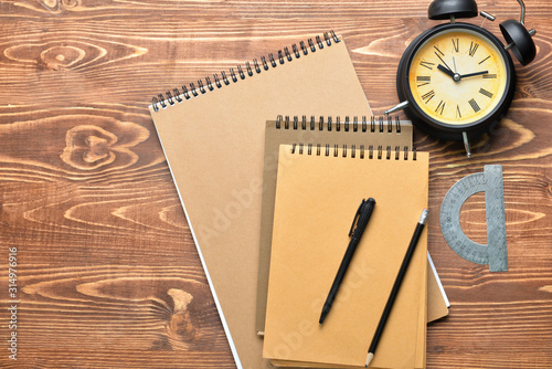 Stylish notebooks with alarm clock and stationery on wooden table